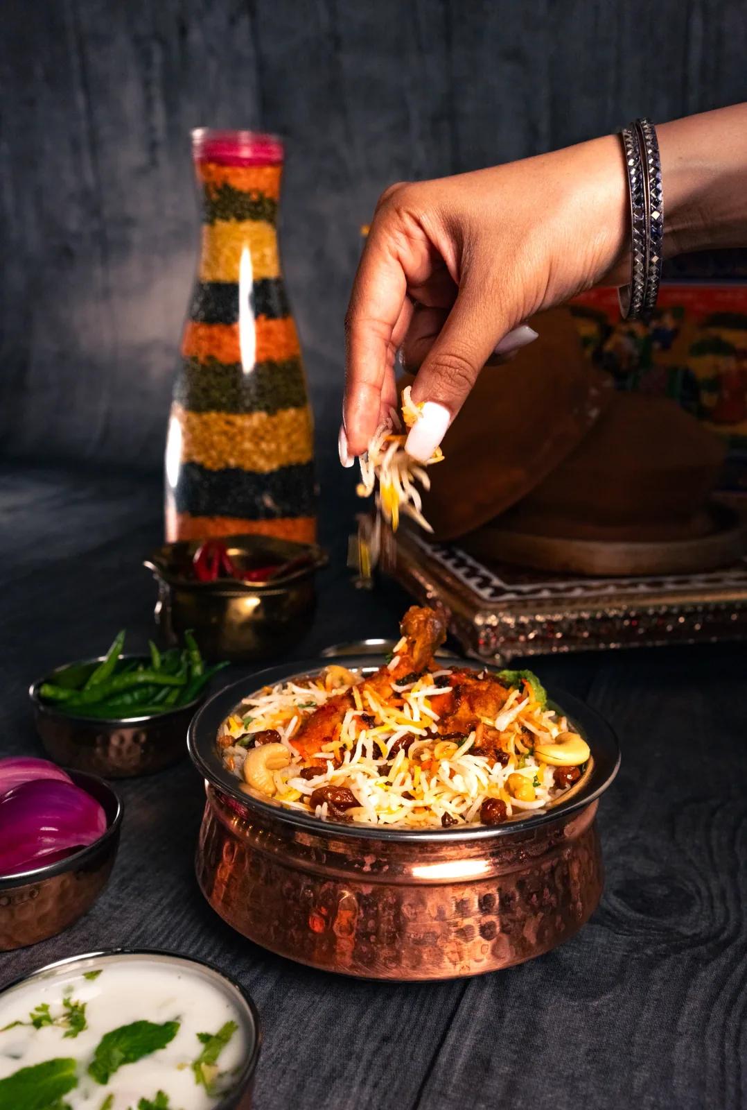 Hand garnishing steaming biryani in a copper pot, food photography by Rahul Chanda, food photographer in Dehradun